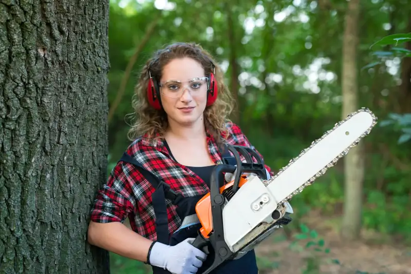Chainsaw operator in ear and eye protection standing beside a large tree