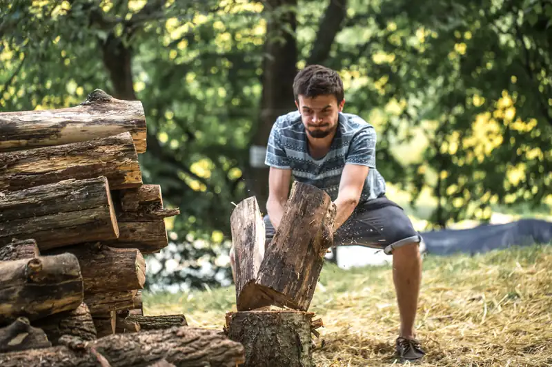 Man splitting a tree log beside a woodpile in a backyard